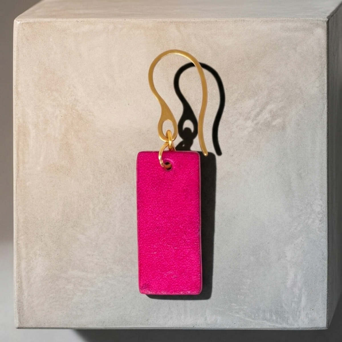Boucle d'oreille en cuir teintée en fuschia très girly et vive, vue de face, suspendue à un crochet doré
