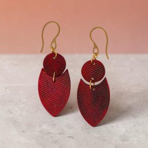 Boucles d'oreilles forme double rond + écu en cuir teinture rouge, texturage lime fine et finition vieillie, vues de face, suspendues à des boucles dorées sur béton