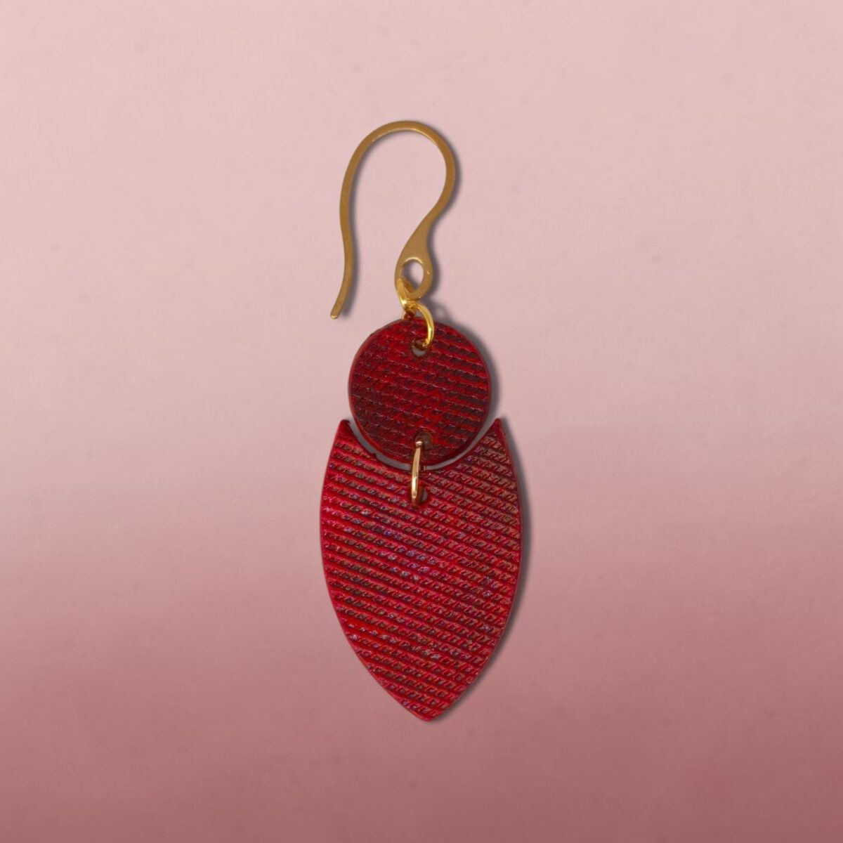 Boucle d'oreille forme double rond + écu en cuir teinture rouge, texturage lime fine et finition vieillie, vue de face, suspendue à une boucle dorée, fond design