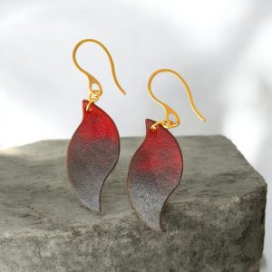 Boucles d'oreilles en cuir teintées en noir et rouge, vues de face, suspendues à des crochets dorés sur pierre