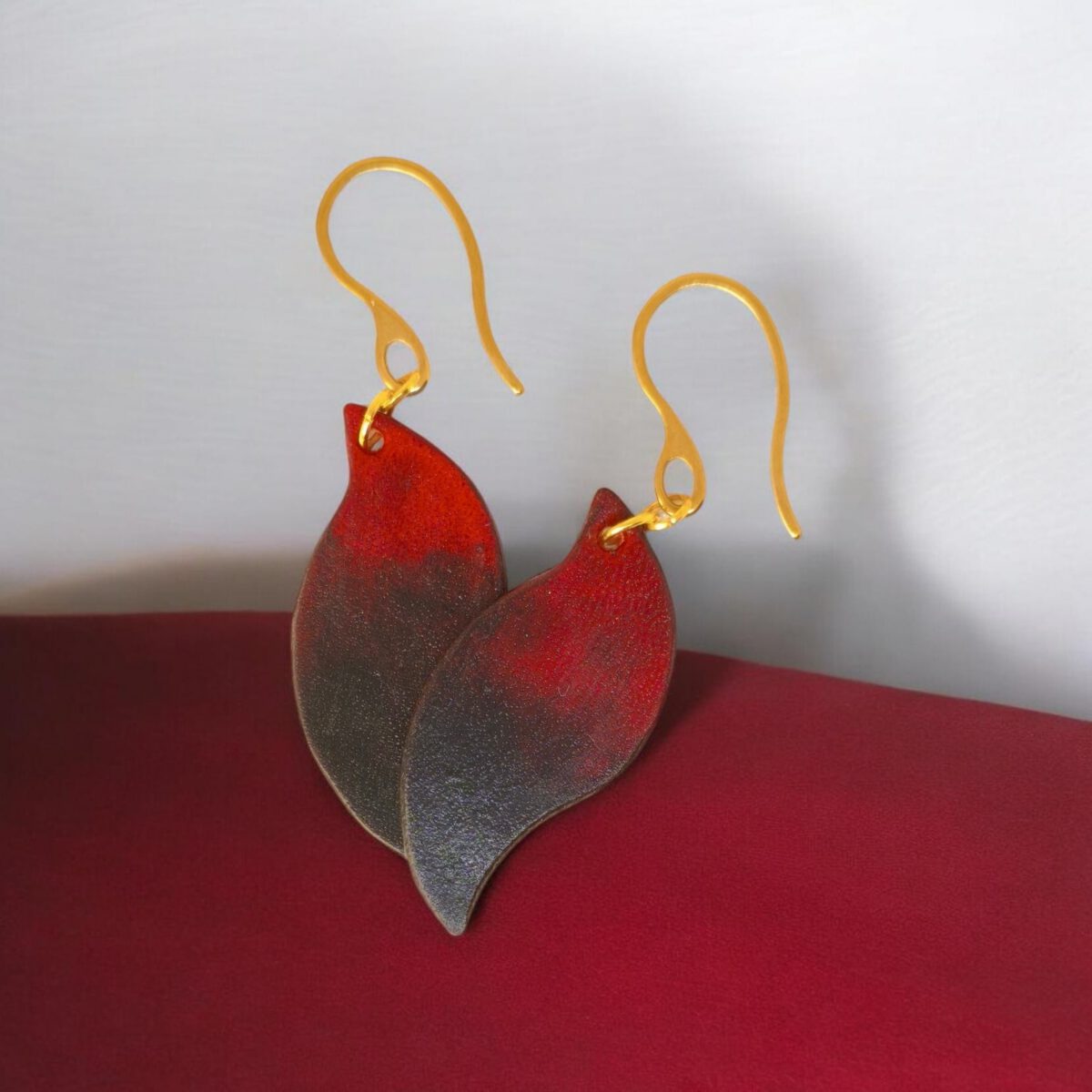 Boucles d'oreilles en cuir teintées en noir et rouge, vues de face se chevauchant, suspendues à des crochets dorés