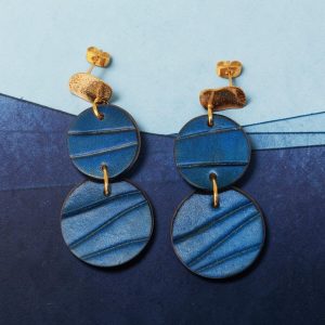 Boucles d'oreilles rondes doubles en cuir teinture bleue, finition galet, vues de face, suspendues à des boucles dorées, fond design