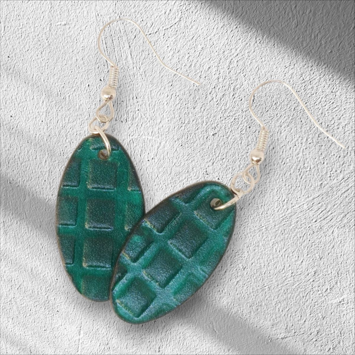 Boucles d'oreilles ovales en cuir teinte vert d'eau, texturage carrés, vues de face se chevauchant, suspendues à des boucles argentées