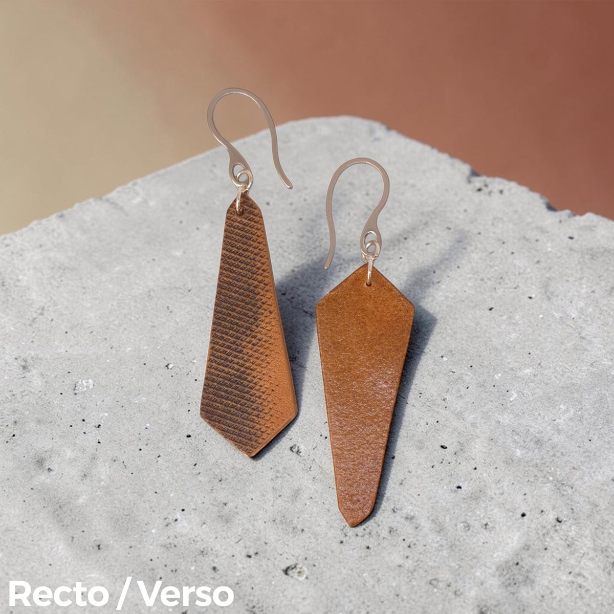 Boucles d'oreilles asymétriques en cuir huilées teinte naturelle, vues recto - verso, suspendues à des crochets argentés sur béton