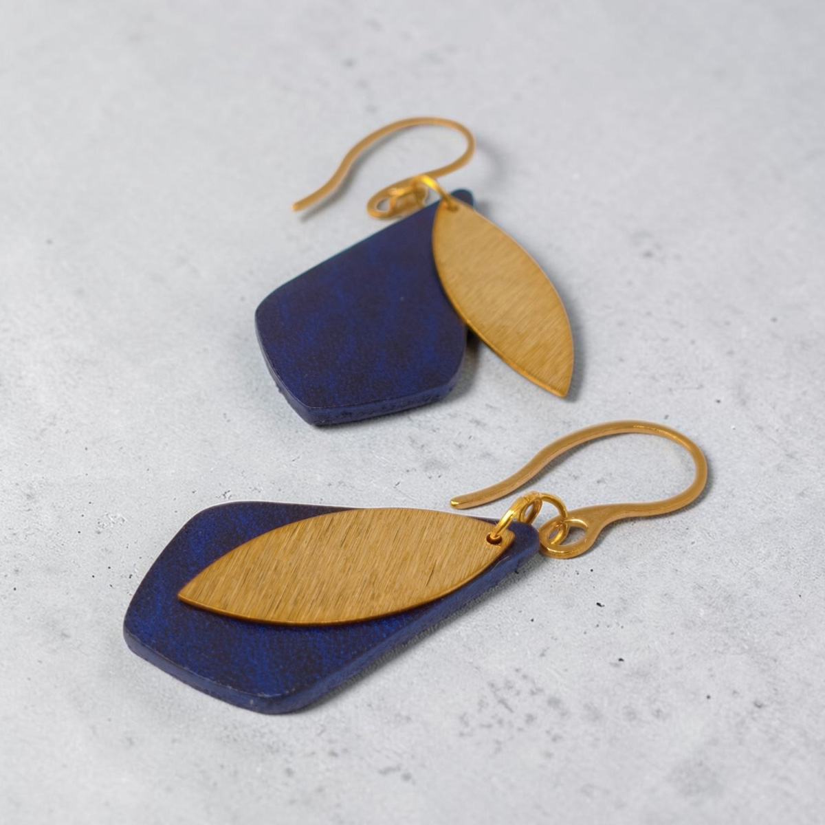 Boucles d'oreilles forme larme en cuir sauvage bleu, taille réduite, finition aniline et pendants dorés brossés, vue latérale, suspendues à des boucles dorées, fond gris